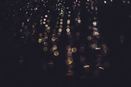 bokeh of lights made by raindrops on a windows illuminated by a torch, abstract background or texture shotの写真素材