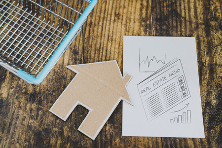 miniature house made of cardboard in shopping basket with real estate trend illustration in notepad,...