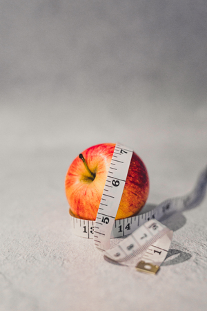 healthy diet concept, red apple with measuring tape around it