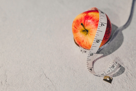 healthy diet concept, red apple with measuring tape around it