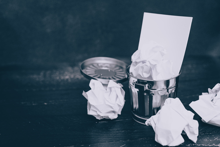 garbage bin on desk setting with notepad and scrunched paper balls, concept of drafting and struggling to write documentsの写真素材