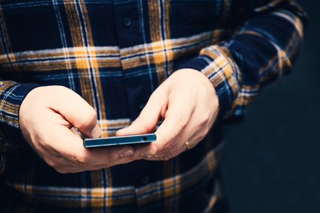 hipster man holding smartphone and tapping on the screen, focus on the hands and dark backgroundの写真素材