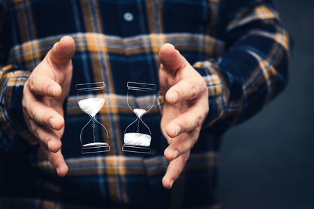 man with hourglass before-after design between his hands, with flannel shiirt and dark backgroundの写真素材