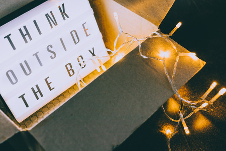 Think outside the box message on lightbox coming out of a parcel with fairy led lights, concept of being unique for successの写真素材
