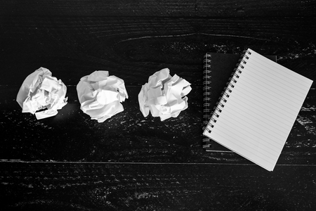 concept of drafting documents and struggling to write a text, set of scrunched paper balls and empty notepad on dark moody backgroundの写真素材