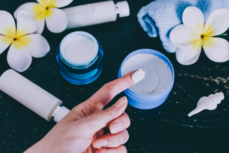 woman's hand touching lotion among other mixed skincare and beauty products with flowers and seashells on dark wood background, concept of luxury spa and pamperingの写真素材