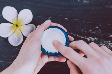 woman's hand touching lotion among other mixed skincare and beauty products with flowers and seashells on dark wood background, concept of luxury spa and pamperingの写真素材