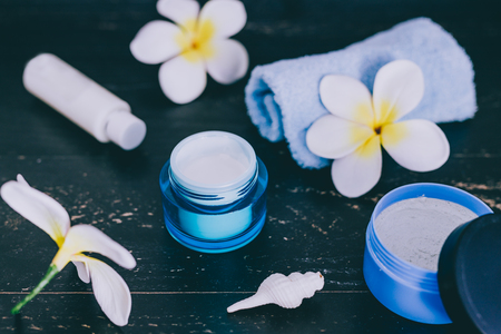 mixed skincare and beauty products with flowers and seashells on dark wood background, concept of luxury spa and pamperingの写真素材