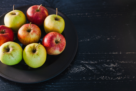 group of organic mixed colours red green and yellow apples on dark plate on black background, concept of selecting the best products and healthy foodの写真素材