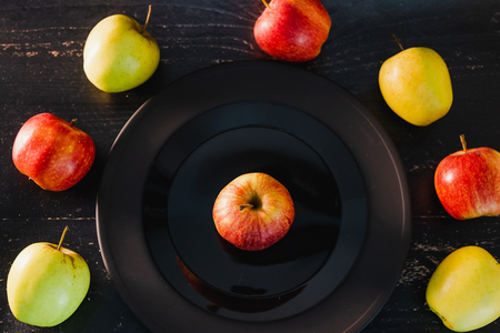 group of organic mixed colours red green and yellow apples on dark plate on black background, concept of selecting the best products and healthy foodの写真素材