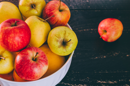 group of mixed red green and yellow apples in a white bowl on dark wood background, concept of organic products and plentinessの写真素材