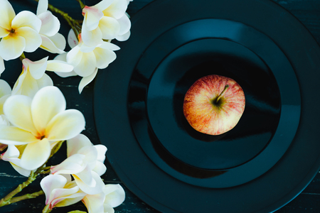 one apple on black plate on dark background and flowers, concept of choosing the best organic productsの写真素材