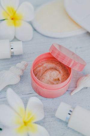 spa inspired set of scrub body lotions surrounded by flowers and seashells on light colored wood, concept of luxury and natural productsの写真素材