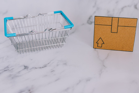 shopping basket with mini cardboard delivery parcel box on marble desk with fairy lights, concept of...