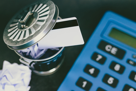payment card thrown in the trash next to huge calculator, concept of learning to spend less and...