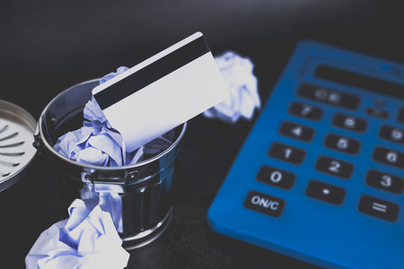 payment card thrown in the trash next to huge calculator, concept of learning to spend less and stick to a budgetの写真素材