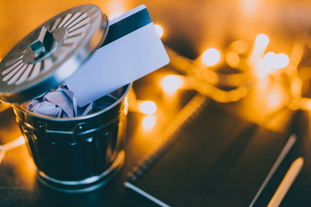 payment card thrown in the trash next to notepad with pencil and fairy lights bokeh,  concept of...