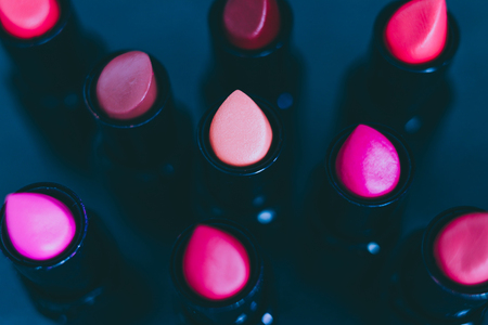 group of red pink and nude lipsticks with different colors and textures on dark table, close-up shot with shallow depth of fieldの写真素材