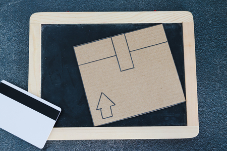 cardboard parcel with blackboard and payment card on concrete desk, concept of shipping and tracking your online deliveriesの写真素材