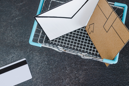 shopping cart with cardboard parcel email envelope and payment card on concrete desk, concept of shipping and tracking your online deliveriesの写真素材