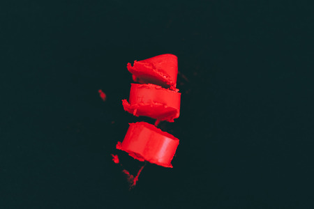 red lipstick cut in chunks on black background, high contrast dark image with vivid reds