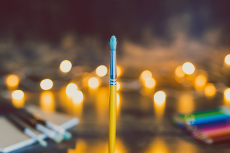 watercolor brush and other art supplies with fairy lights bokeh shot at shallow depth of field with golden tones, concept of creativityの写真素材