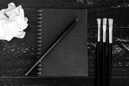 black notepad on dark desk with brushes and scrunched paper balls, concept of creativity and inspirationの写真素材