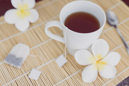 cup of dark tea on bamboo placemat with spoon and flowers all around, concept of detox or relaxing habitsの写真素材