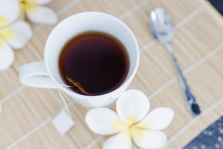cup of dark tea on bamboo placemat with spoon and flowers all around, concept of detox or relaxing habitsの写真素材