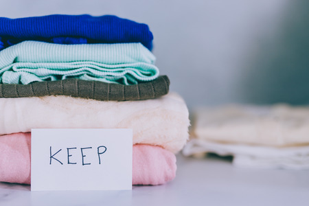 decluttering and tidying up concept: piles of tshirts and clothes being sorted into Keep Discard and Donate categoriesの写真素材