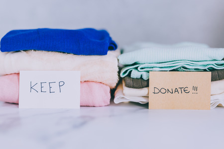 decluttering and tidying up concept: piles of tshirts and clothes being sorted into Keep Discard and Donate categoriesの写真素材