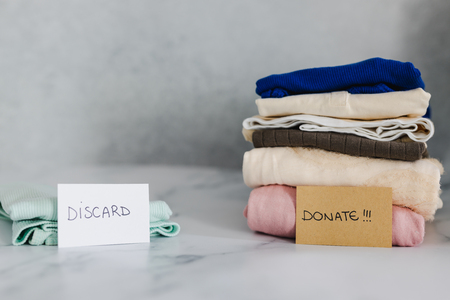 decluttering and tidying up concept: piles of tshirts and clothes being sorted into Keep Discard and...