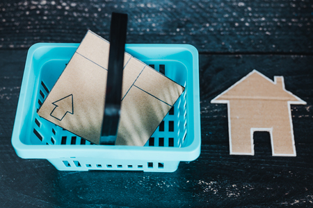 buying decor items or furniture concept: shopping basket with parcel and small cardboard house next to itの写真素材