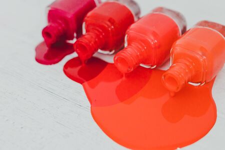 nail polish bottles in different shades of red to orange and purple spilling color on wooden surface, concept of cosmetics industry and manicureの写真素材