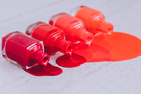 nail polish bottles in different shades of red to orange and purple spilling color on wooden surface, concept of cosmetics industry and manicureの写真素材