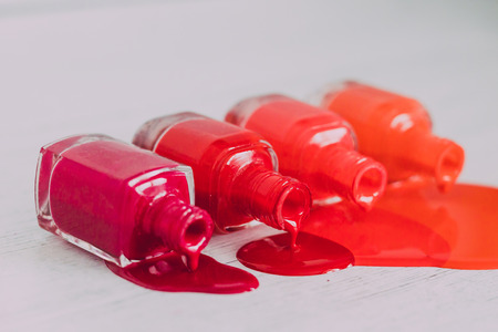 nail polish bottles in different shades of red to orange and purple spilling color on wooden...