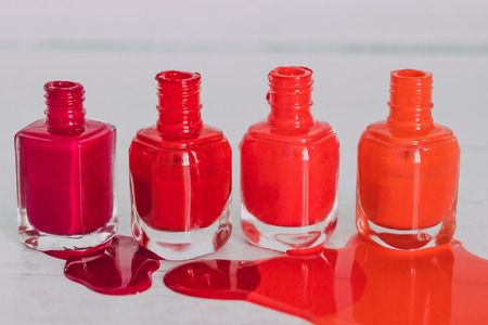 nail polish bottles in different shades of red to orange and purple spilling color on wooden surface, concept of cosmetics industry and manicureの写真素材