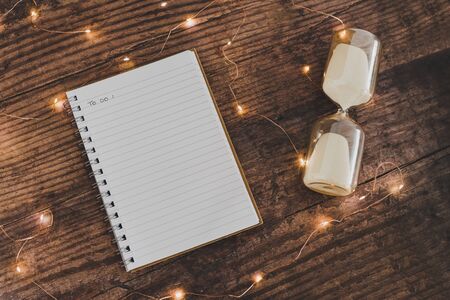 time to get things done conceptual image with hourglass and to do list notebook surrounded by fairy lights bokeh on wooden office deskの写真素材