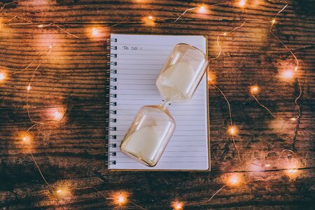 time to get things done conceptual image with hourglass and to do list notebook surrounded by fairy lights bokeh on wooden office deskの写真素材