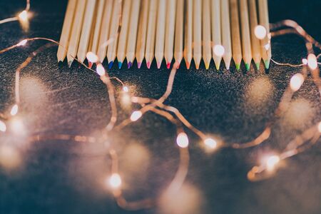 set of coloured pencils on desk with fairy lights shot at shallow deph of field, concept of art and craft projectsの写真素材