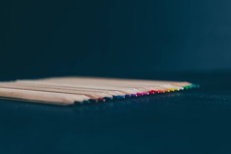set of coloured pencils on desk on dark background shot at shallow deph of field, concept of art and...