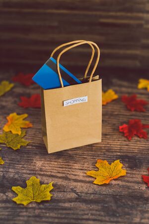 shopping bag with payment card on wooden table surrounded by autumn leaves, concept of seasonal trendsの写真素材