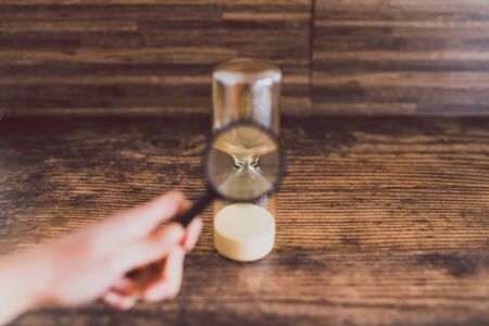hand holding magnifying glass analyzing time passying by with an hourglass, concept of time...