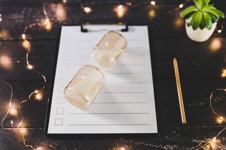 clipboard with blank list with cases to tick off on wooden desk with hourglass, concept of time...