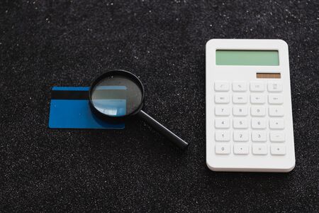payment card and magnifying glass analyzing it with calculator, customer spending habits concept