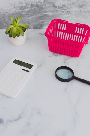 pink shopping basket on marble desk with magnifying glass and calculator, concept of analyzing your...