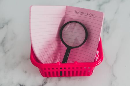 pink shopping basket on marble desk with magnifying glass in it,  concept of analyzing your expenses and budgetingの写真素材