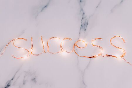 Success message made of fairy lights on marble desk background, conceptual still-lifeの写真素材
