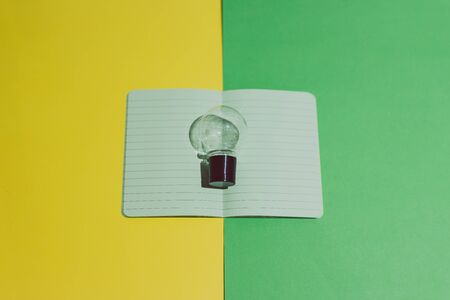 open notebook with blank green pages with lightbulb above it on contrasting yellow and green...