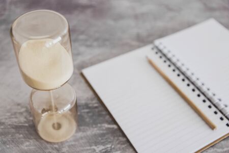 concept of business deadlines and productivity, notebook on office desk with hourglass next to itの写真素材